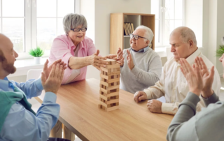 Group of senior people sitting at table in nursing home and playing Jenga together.