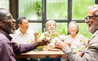 Group of diverse seniors enjoying a meal, laughing and toasting with wine glasses.