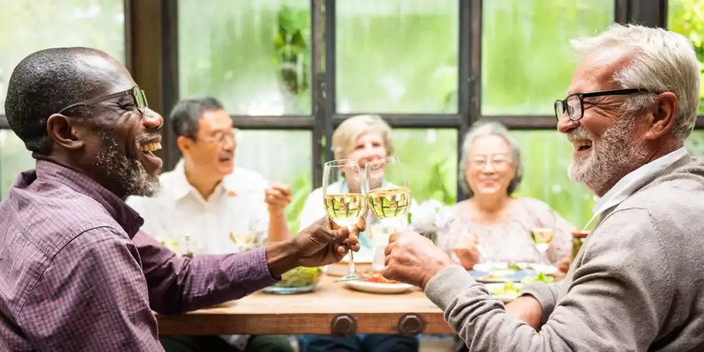 Group of diverse seniors enjoying a meal, laughing and toasting with wine glasses.