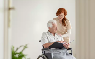 Caregiver supporting paralyzed elderly man in a wheelchair with photo album